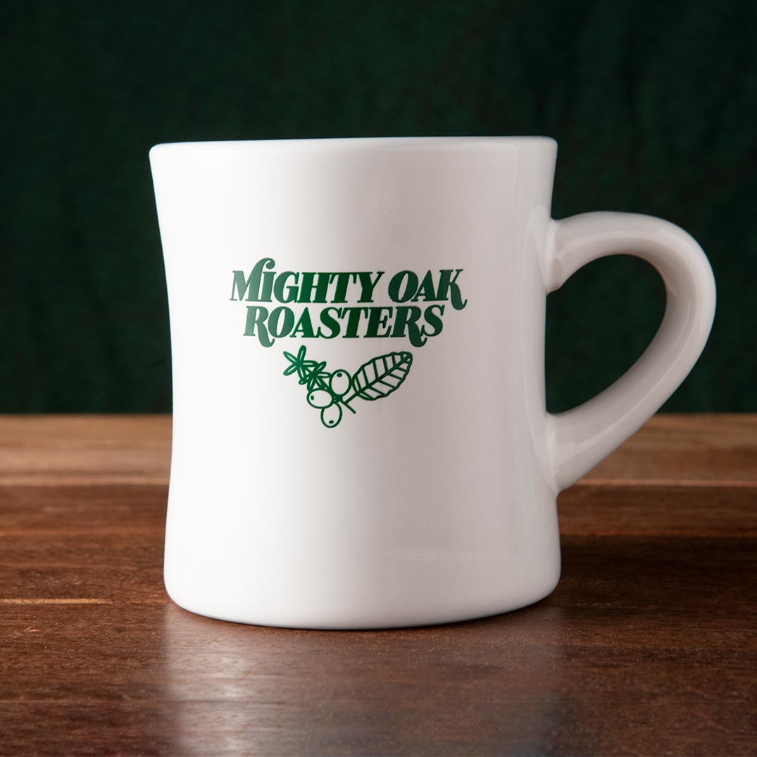 A white ceramic diner mug with the text 'MIGHTY OAK ROASTERS' printed in green. The mug has a retro shape and is placed on a wooden surface.